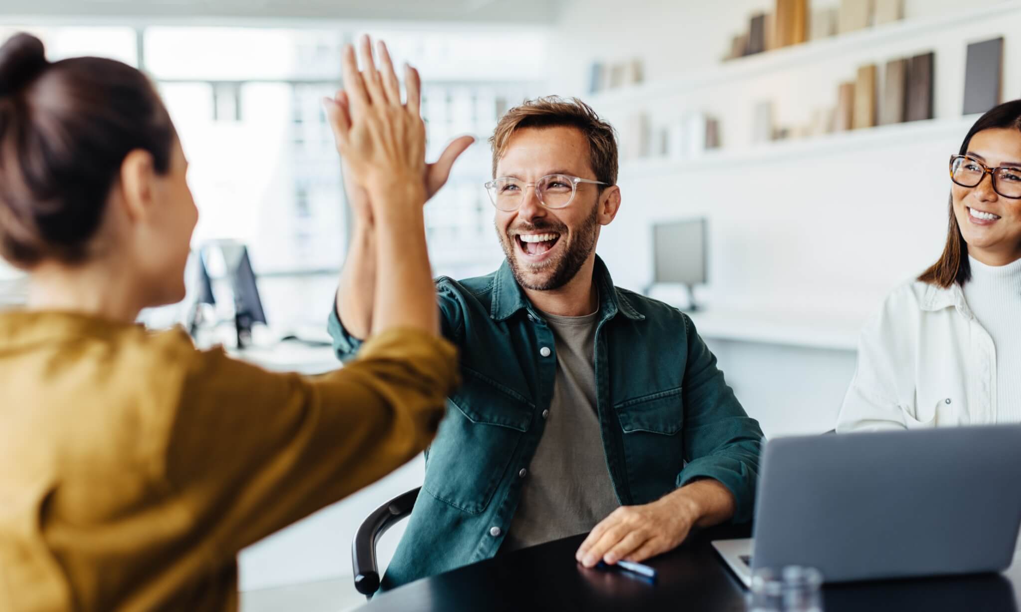 Woman giving a man a highfive as they sit around a desk.